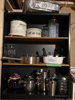Overview of multiple shelves showing various pots, pans, dishes including Henckels fry/sauce pan, CorningWare dishes, glass canisters, and baking materials.