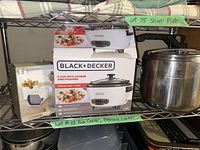 Rice cooker box with Black & Decker branding, alongside Lagostina pressure cooker and potato chipper box on metal shelving.