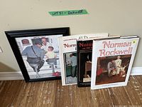 Photo showing four Norman Rockwell art books standing next to a small framed print depicting a policeman talking to a boy at a counter in a diner.