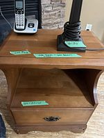 Close-up of wooden side table showing the open shelf and drawer with metal handle, including measurement tags.