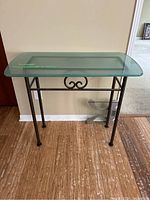 Full view of small glass top table showing metal legs and decorative front scroll design