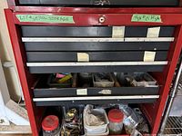 Front view of red metal tool storage unit with drawers partly open showing hardware containers inside.