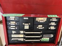 Full view of red metal tool storage with multiple black labeled drawers, showing wear and tear.