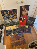 Overview photo showing all eight acrylic paintings demonstrating varying sizes and themes, placed on a hardwood floor in front of white doors.