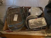 Overview of assorted kitchen bakeware in cardboard box containing glass rectangular baking dishes, Corningware, aluminum foil pans