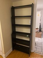 Front view of black engineered wood bookshelf against wall showing five shelves.