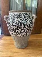 Full frontal view of the ceramic vase showing the black scrollwork design and two decorative handles.