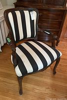Front angle view of the wood frame armchair with black and white striped upholstery showing carved armrest and legs.