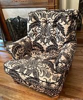 Front angled view showing bold tropical motif fabric upholstery on cushioned backrest, armrests and seat, with wooden legs.