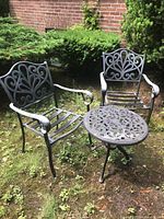 Two black decorative metal chairs and round table on outdoor ground