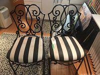 Two metal framed chairs with black and white striped fabric seats, decorative scrollwork backrests, shown side by side on patterned rug.