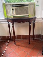 Front view of the Bombay Company wooden console table below a window with air conditioner.