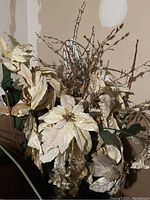 Close-up photo of dried seasonal florals showing cream-colored poinsettia flowers with gold accents and dried twigs inside a box