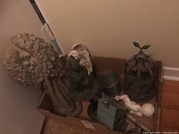 Box with large angel figurine with wings, a ballerina figurine, metal bucket, floral metal container, and other ceramic pieces inside.