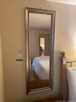 Full view of rectangular mirror hanging on wall beside bed, showing clear mirror image and distorted reflection of bedroom area.
