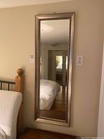Full view of the framed rectangular mirror 18x50 inches mounted on a wall next to a bed and an electrical outlet.