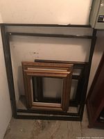 Six stacked wooden picture frames leaning against a wall in basement.