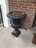 Front view of the black metal urn planter against a brick wall.