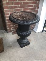 Full front view of black metal urn on concrete porch against brick wall