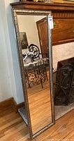 Full view of rectangular wall mirror with decorative leaf pattern wood frame leaning against wall.