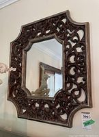 Full view of the wall mirror showing its ornate carved wooden frame with scroll and floral detailing and beveled glass.