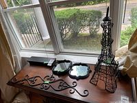 Photo of wood stand, two wood frame quatrefoil shape mirrors, metal wall art scrollwork, and wire Eiffel Tower sculpture on wood table by window.