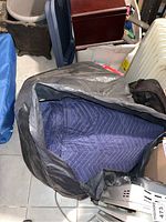 One image showing multiple dark blue quilted moving blankets inside a large black bag, situated in a basement area with other household items.