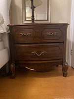 Front view of the wooden nightstand showing top surface with a lamp and three drawers with brass handles.
