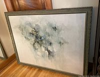 Painting leaning against a wall, showing the full wooden frame and glass front, with soft abstract watercolor design.