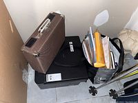 Side view showing the brown hard-sided carrying case on top of the printer with a bag and papers beside it