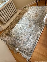 Full view of the rectangular floral motif area rug on wood floor showing overall pattern, color, and fringe wear.