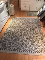 Larger 7x5 feet rug with beige and brown geometric floral pattern laid on wood floor near kitchen area.