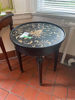 Angled view of the round side table showing the floral design on the black top and dark wood legs.