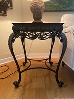 Side view of the side table showing ornate black metal legs with leaf and scroll details