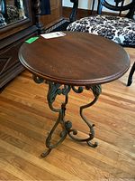 Angle showing round wood top and ornate green metal base with scroll and leaf motifs