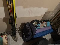 Rossignol skis with bindings standing against wall next to blue equestrian bag, purple yoga mat, and boxed pool float visible on bench.