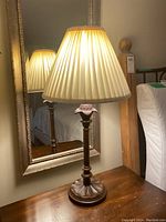 Full view of one lamp including wooden base, flower-shaped detail, and pleated lampshade.