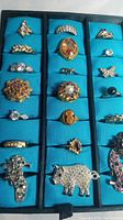 Full view of 21 rings in display case showing variety of stones, metals and styles.