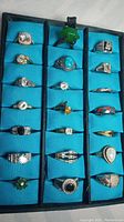 Tray of 21 non-precious metal rings with various stones and crystals on blue padded cushions arranged in rows