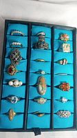 Top view of 21 assorted vintage non-precious rings in a black display tray with blue fabric inserts.