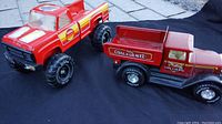 Two red vintage metal toy trucks, Tonka pickup and Nylint dump truck on pavement and black cloth