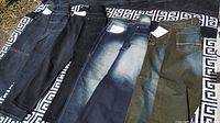 Four pairs of men's jeans laid out showing full length and fabric colors from black to olive green, highlighting wear and style.