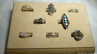 Eight vintage sterling silver rings arranged on beige felt display board in two rows, showing variety of sizes and styles.