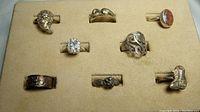 Top-down photo showing all 8 vintage sterling silver rings laid out in a beige holder with slots; rings have various designs and stones including clear CZ and orange glass/stone.