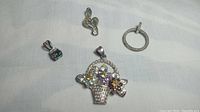 Four sterling silver pendants displayed on a white cloth: musical note with diamonds, CZ circle pendant, flower basket pendant with colored stones, mystic topaz pendant with CZ accents.