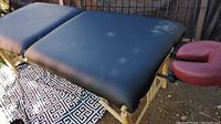 Full view of black massage table set up outdoors with burgundy face cradle attached