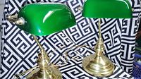 Pair of mid-century green glass banker’s lamps with brass bases displayed against patterned cloth.