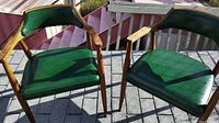 Pair of vintage Mid Century Modern green vinyl chairs with wooden frames, armrests, and tapered legs shown outdoors on pavement.