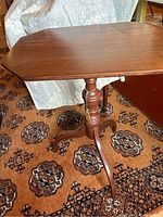 Side view of the antique wooden pedestal candle stand showing the turned pedestal and tripod base on patterned carpet.