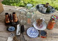 Photo of lot showing copper baby shoe bookends, vintage canning jars, metal and glass kitchen items on wooden surface outdoors